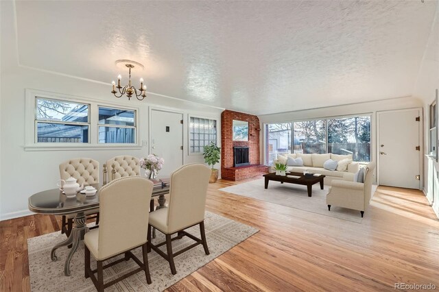 dining area featuring a brick fireplace, a textured ceiling, an inviting chandelier, and light hardwood / wood-style flooring