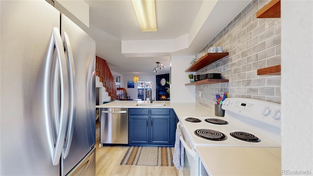 kitchen with sink, light hardwood / wood-style flooring, blue cabinetry, stainless steel appliances, and kitchen peninsula