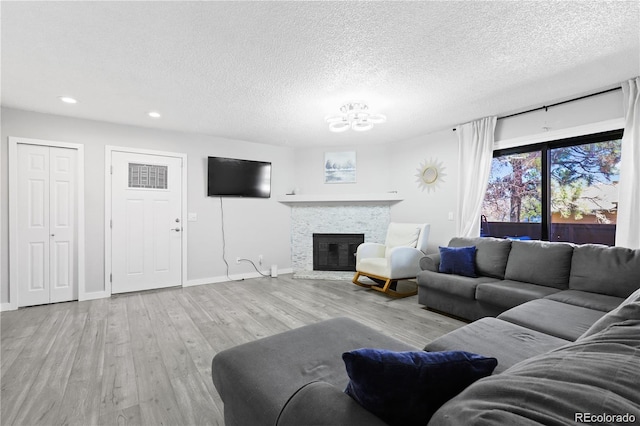 living room featuring baseboards, a chandelier, a stone fireplace, wood finished floors, and a textured ceiling