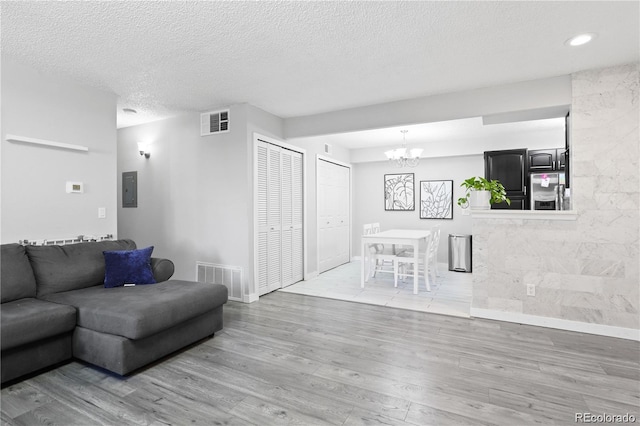 living room featuring an inviting chandelier, wood finished floors, visible vents, and a textured ceiling