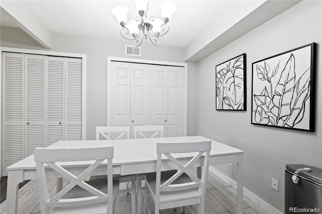 dining space with a notable chandelier, wood finished floors, visible vents, and a textured ceiling