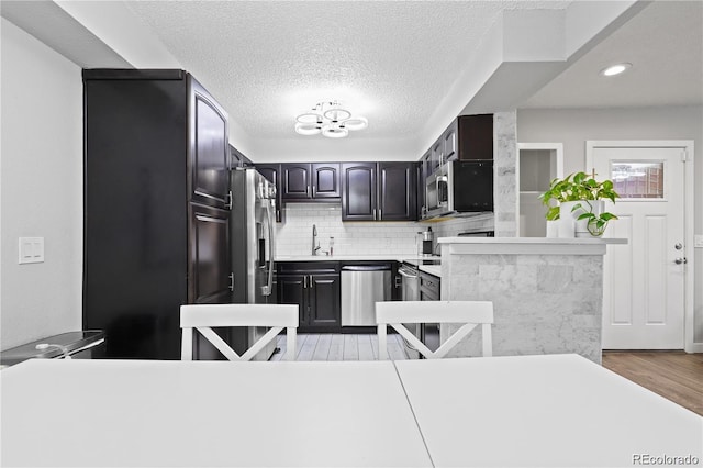 kitchen with tasteful backsplash, light wood-type flooring, light countertops, stainless steel appliances, and a sink