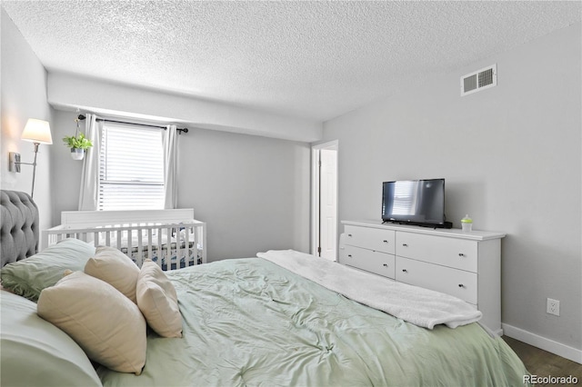 bedroom featuring visible vents, a textured ceiling, dark wood-type flooring, and baseboards