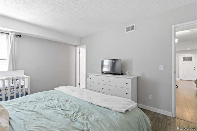 bedroom featuring visible vents, a textured ceiling, baseboards, and wood finished floors