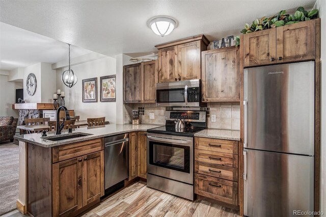 kitchen featuring light stone countertops, a peninsula, a sink, appliances with stainless steel finishes, and backsplash