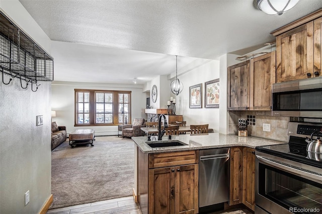 kitchen with tasteful backsplash, open floor plan, appliances with stainless steel finishes, a peninsula, and a sink