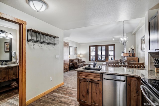 kitchen featuring a sink, light stone counters, open floor plan, a peninsula, and dark wood-style flooring