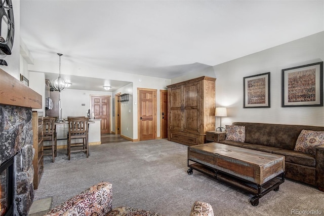 carpeted living area featuring a stone fireplace and an inviting chandelier