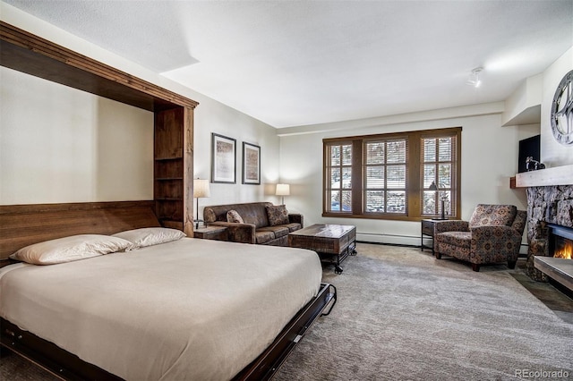 bedroom with a baseboard heating unit, a stone fireplace, and carpet flooring