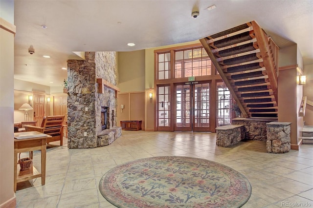 living area with a stone fireplace, french doors, stairs, and a high ceiling