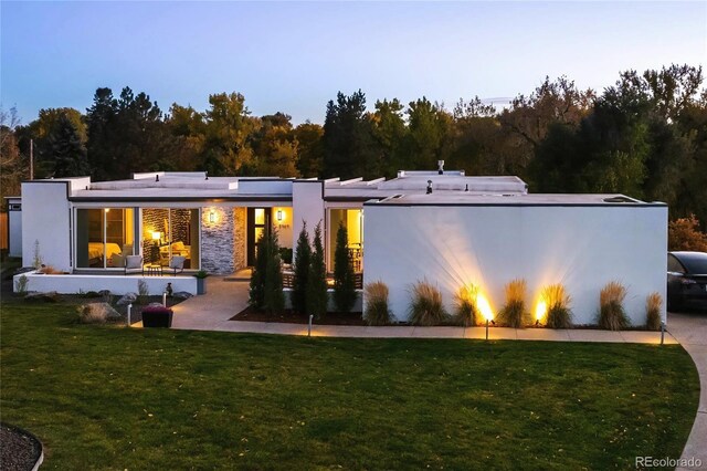 back of house at dusk with stucco siding and a yard