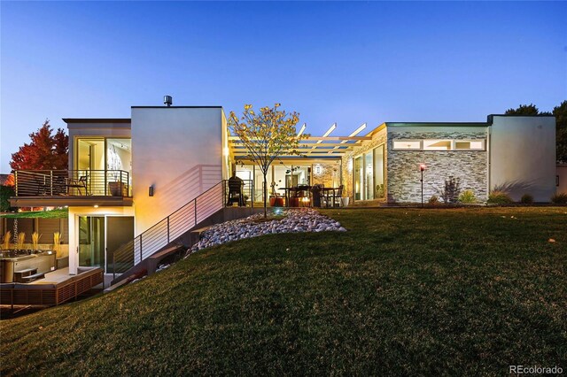 back of house with a pergola, stone siding, a patio area, a balcony, and a yard