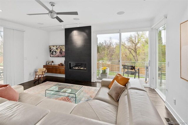 living room with a large fireplace, ceiling fan, baseboards, and wood finished floors