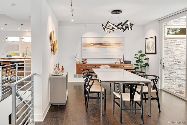 dining room featuring track lighting, dark wood-style flooring, baseboards, and a notable chandelier