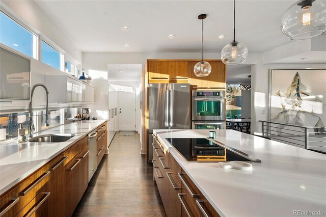 kitchen featuring brown cabinetry, modern cabinets, light countertops, a sink, and appliances with stainless steel finishes