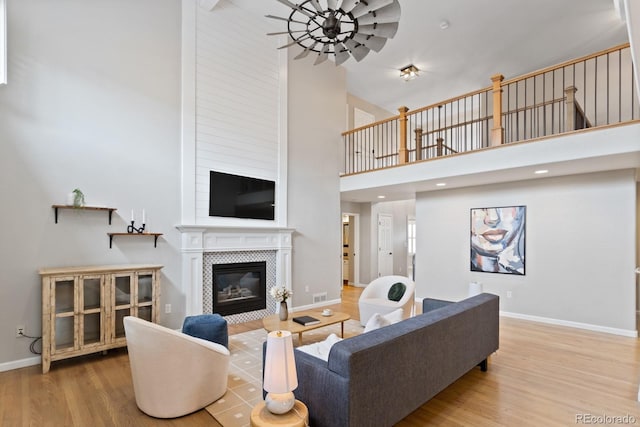 living area featuring wood finished floors, a towering ceiling, a fireplace, ceiling fan, and baseboards