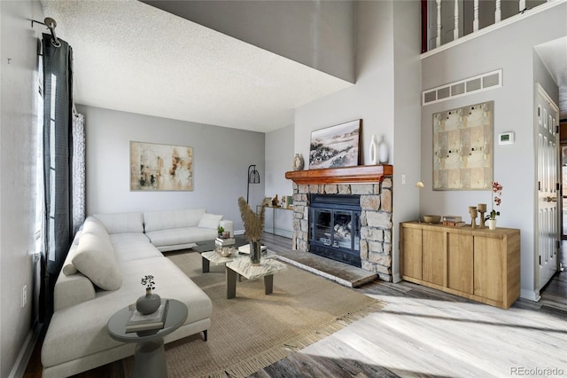 living room featuring wood-type flooring, plenty of natural light, a stone fireplace, and a textured ceiling