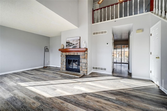 unfurnished living room with a high ceiling, wood-type flooring, a textured ceiling, and a stone fireplace