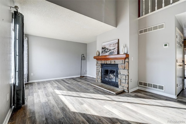 unfurnished living room with a textured ceiling, a towering ceiling, hardwood / wood-style flooring, and a stone fireplace