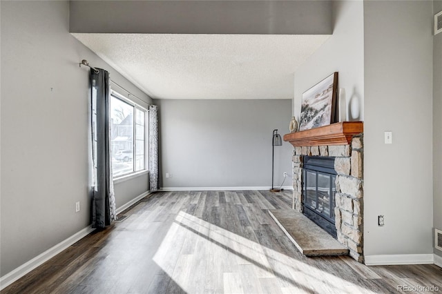 living room featuring wood-type flooring, a stone fireplace, and a textured ceiling