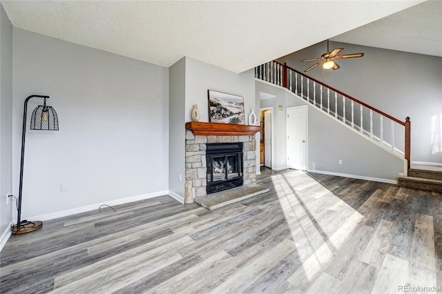 unfurnished living room with a textured ceiling, ceiling fan, wood-type flooring, and a stone fireplace