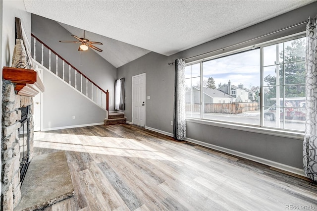 unfurnished living room featuring ceiling fan, vaulted ceiling, a fireplace, light hardwood / wood-style flooring, and a textured ceiling