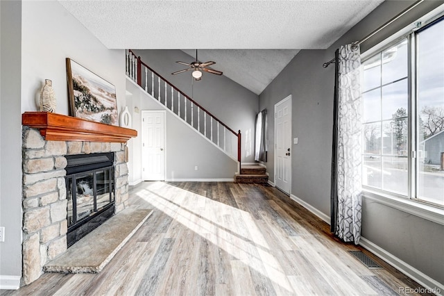 unfurnished living room with hardwood / wood-style floors, a stone fireplace, ceiling fan, a textured ceiling, and vaulted ceiling