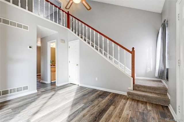 stairs featuring a high ceiling, ceiling fan, and hardwood / wood-style floors