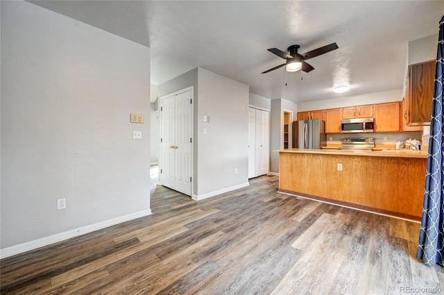 kitchen with ceiling fan, kitchen peninsula, appliances with stainless steel finishes, and dark hardwood / wood-style flooring