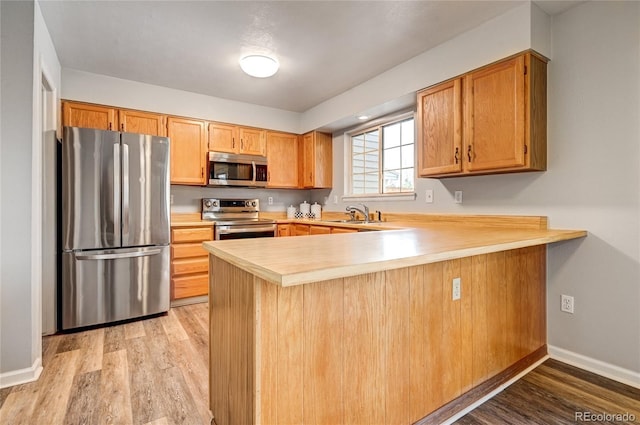 kitchen featuring kitchen peninsula, appliances with stainless steel finishes, sink, and light hardwood / wood-style flooring