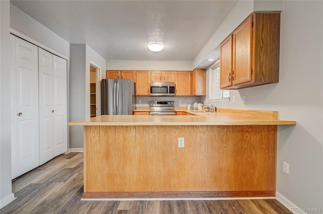 kitchen featuring dark wood-type flooring, appliances with stainless steel finishes, kitchen peninsula, and sink