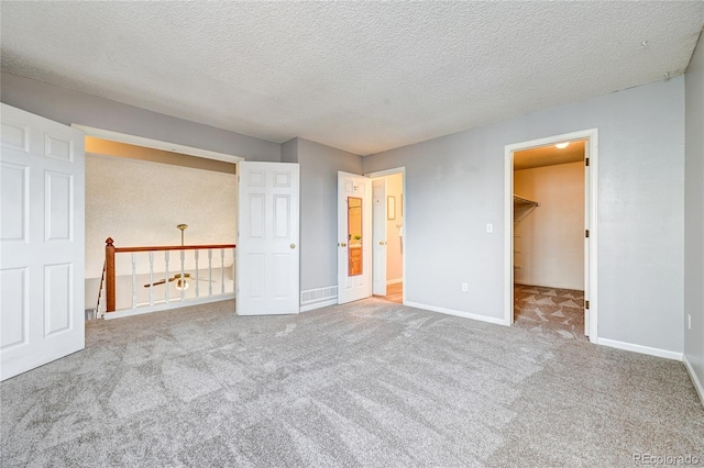 unfurnished bedroom featuring a walk in closet, a closet, light colored carpet, and a textured ceiling