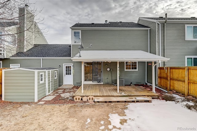 snow covered back of property featuring a storage unit and a wooden deck