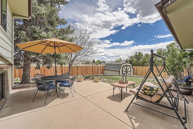 view of patio featuring a fenced backyard, a storage unit, outdoor dining space, and an outdoor structure