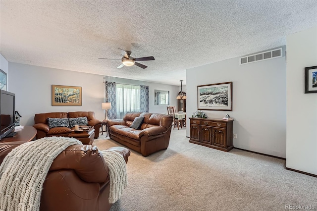 living room featuring ceiling fan, light colored carpet, a textured ceiling, baseboards, and visible vents