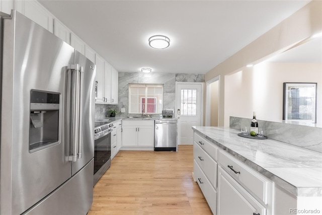 kitchen with white cabinets, light wood finished floors, light stone counters, a sink, and appliances with stainless steel finishes
