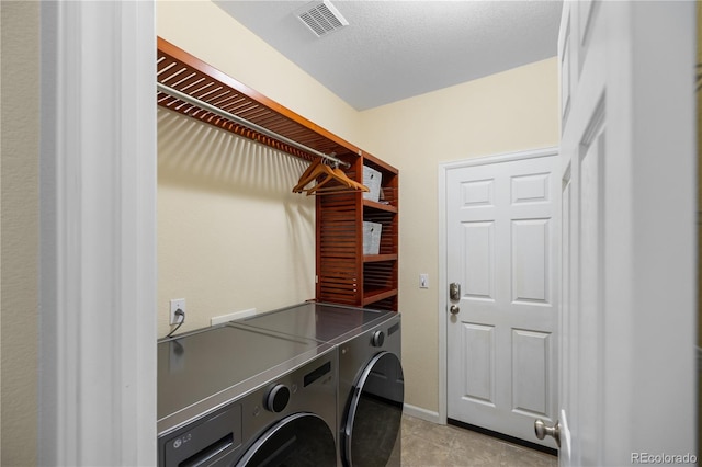 clothes washing area with light tile patterned flooring, a textured ceiling, and washer and clothes dryer