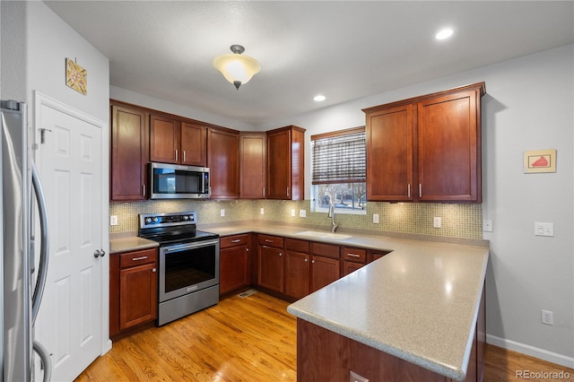 kitchen with sink, light wood-type flooring, kitchen peninsula, and stainless steel appliances