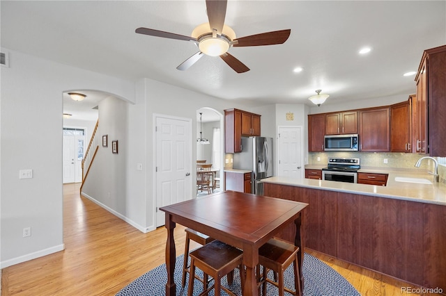 kitchen with stainless steel appliances, decorative backsplash, sink, kitchen peninsula, and light wood-type flooring