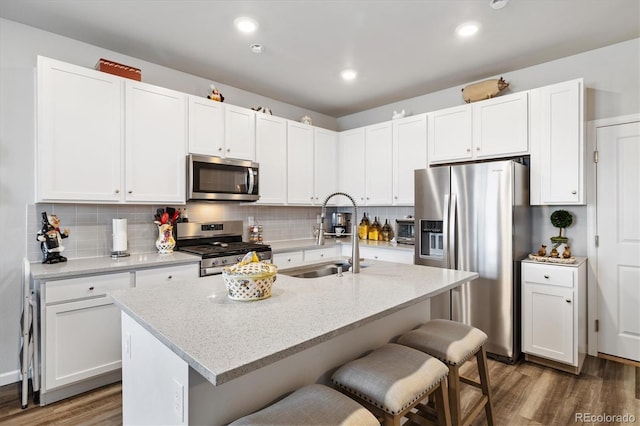 kitchen with a sink, dark wood finished floors, stainless steel appliances, a kitchen bar, and backsplash