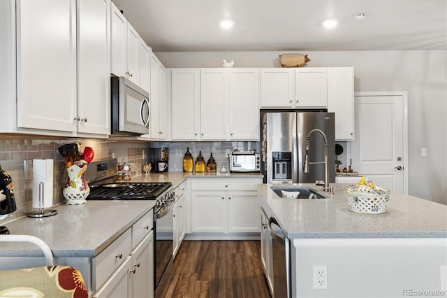 kitchen with a kitchen island with sink, light stone countertops, a sink, white cabinets, and stainless steel appliances