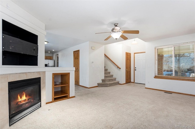 unfurnished living room with ceiling fan, a fireplace, and light colored carpet