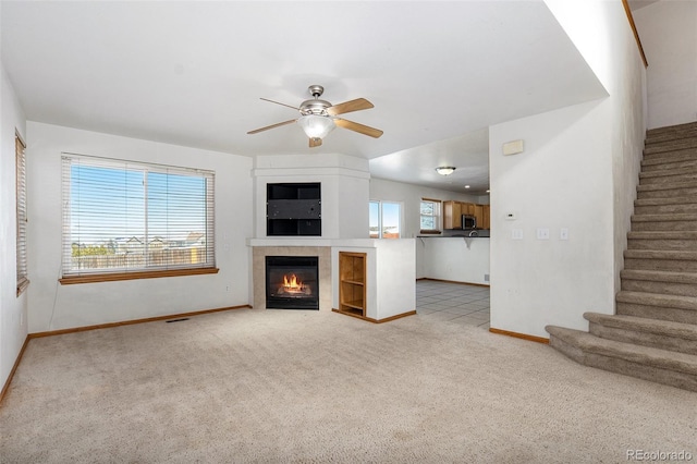 unfurnished living room with ceiling fan, light colored carpet, and a fireplace