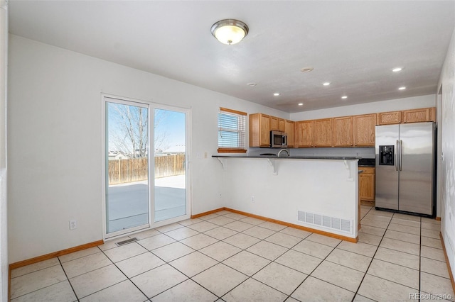 kitchen with a breakfast bar, sink, light tile patterned floors, appliances with stainless steel finishes, and kitchen peninsula