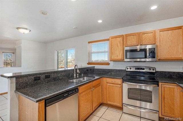 kitchen featuring kitchen peninsula, stainless steel appliances, dark stone countertops, and sink