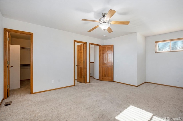 unfurnished bedroom with a walk in closet, ceiling fan, a closet, and light colored carpet