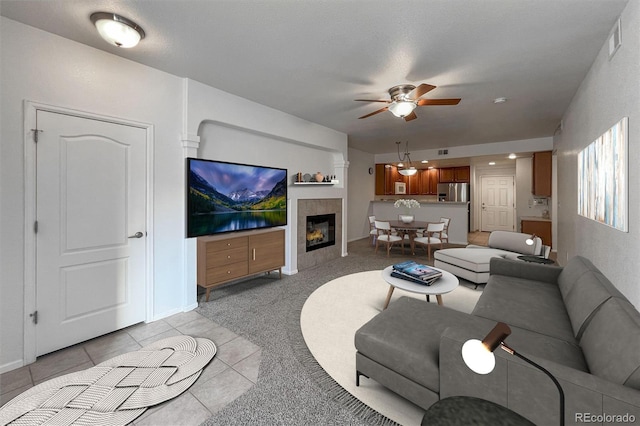 living room featuring a tile fireplace, light carpet, and ceiling fan