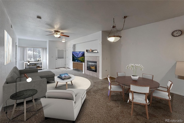 carpeted living room featuring ceiling fan, a fireplace, and a textured ceiling