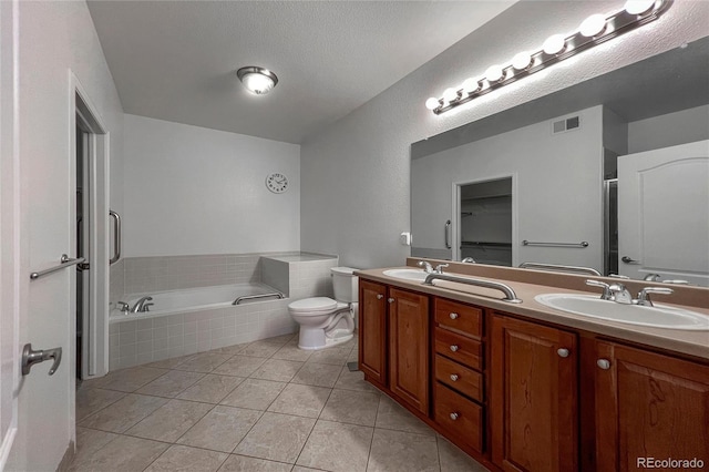 bathroom with tile patterned flooring, tiled tub, vanity, and toilet