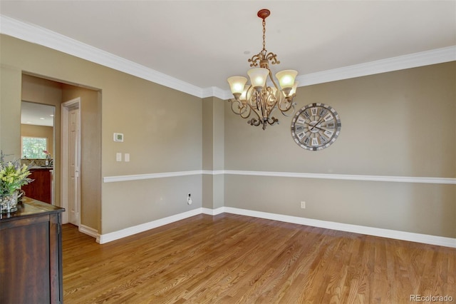 spare room with wood-type flooring, ornamental molding, and a chandelier